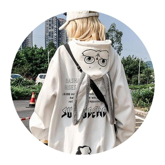 Person wearing a white hoodie with text and graphics, standing outdoors.