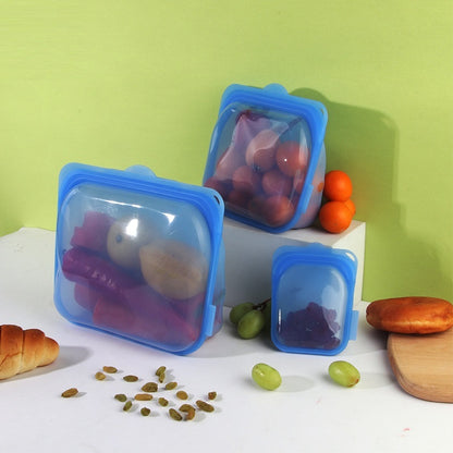 Blue silicone food storage bags with fruits and bread on a white surface with a green background