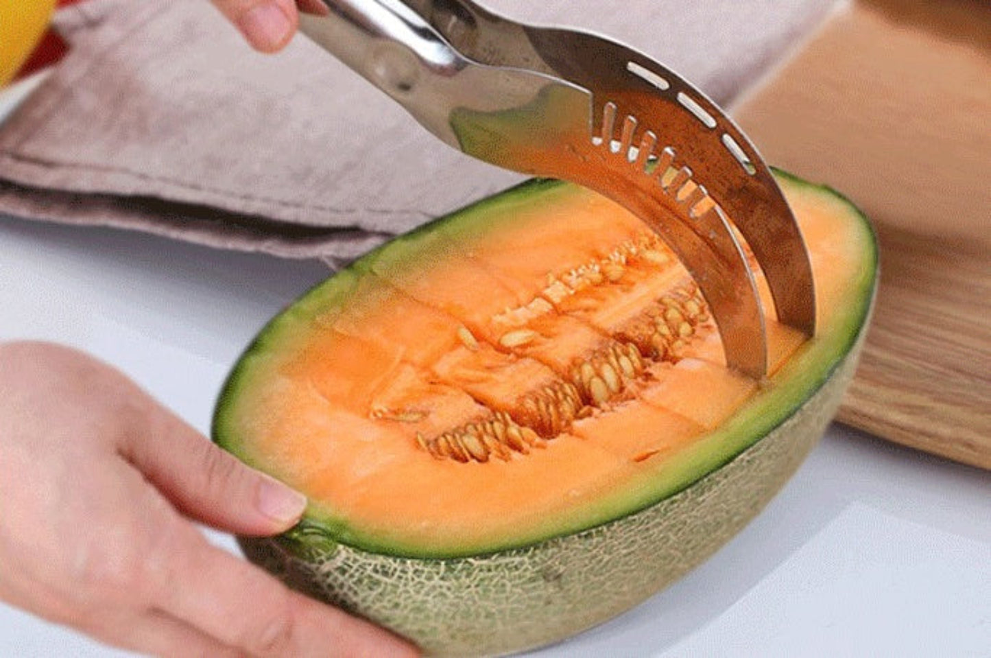 Person using a melon baller to scoop out a cantaloupe on a white surface.