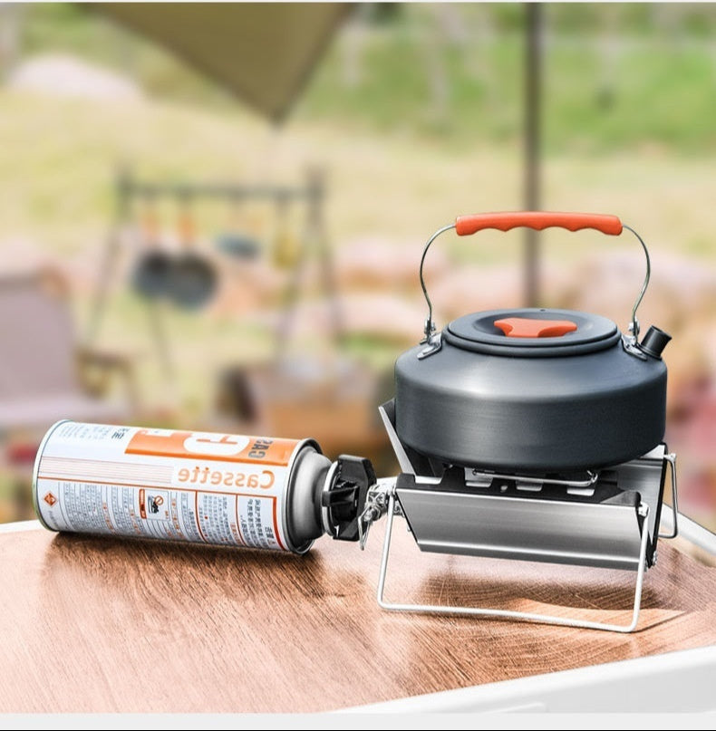 Outdoor setting with a camping stove, kettle, and canister on a wooden surface.