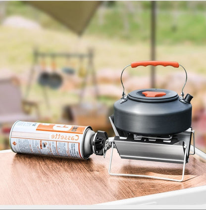 Outdoor setting with a camping stove, kettle, and canister on a wooden surface.