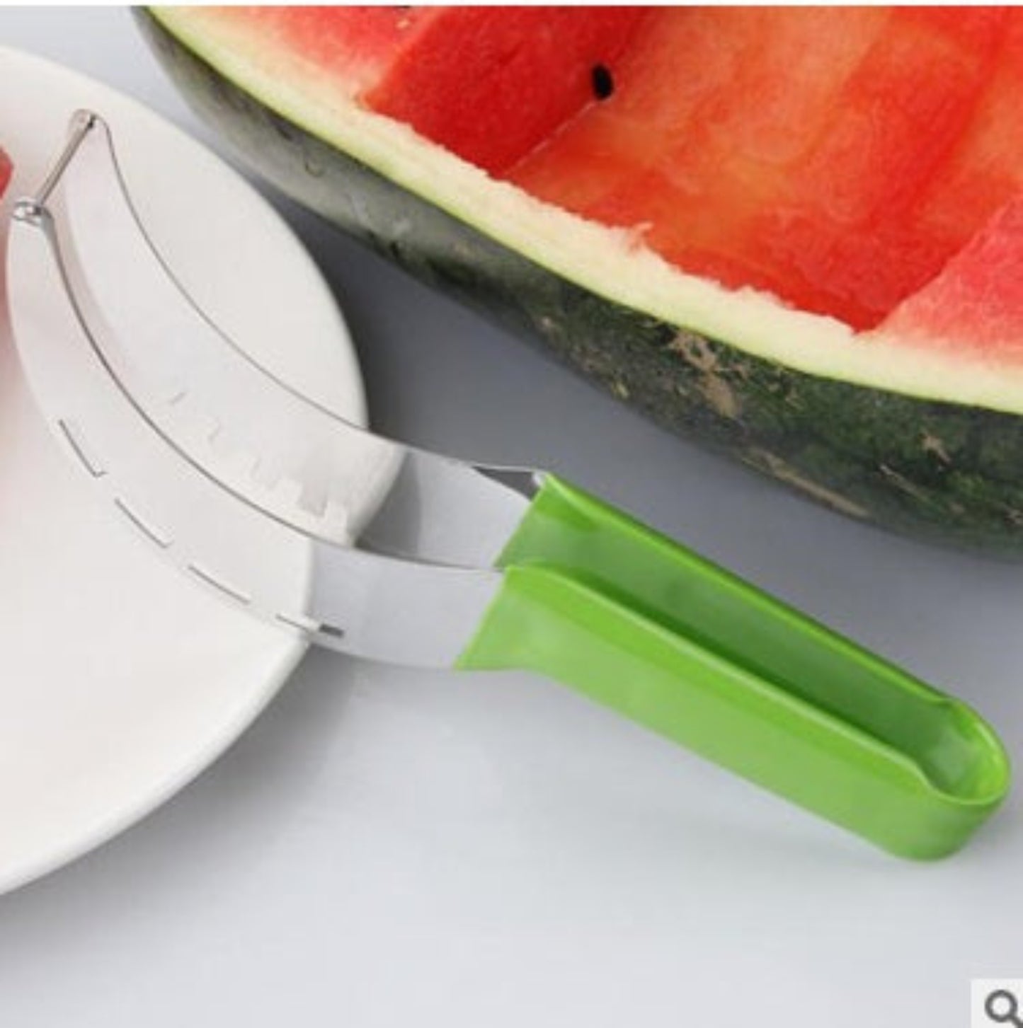 Watermelon slicer with a green handle next to a watermelon on a white background