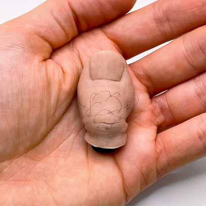 Hand holding a small beige object with a textured surface and black markings on a light background
