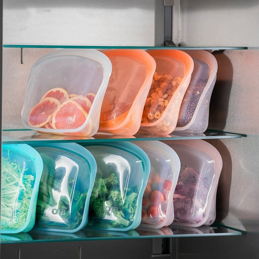 Reusable silicone food storage bags with different contents on a refrigerator shelf.