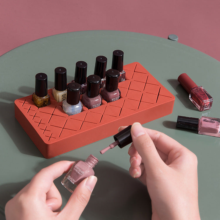 Person applying nail polish from a red holder with multiple bottles on a green surface.