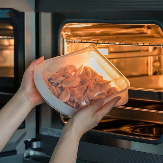 Person holding a container of shrimp in front of an open oven.