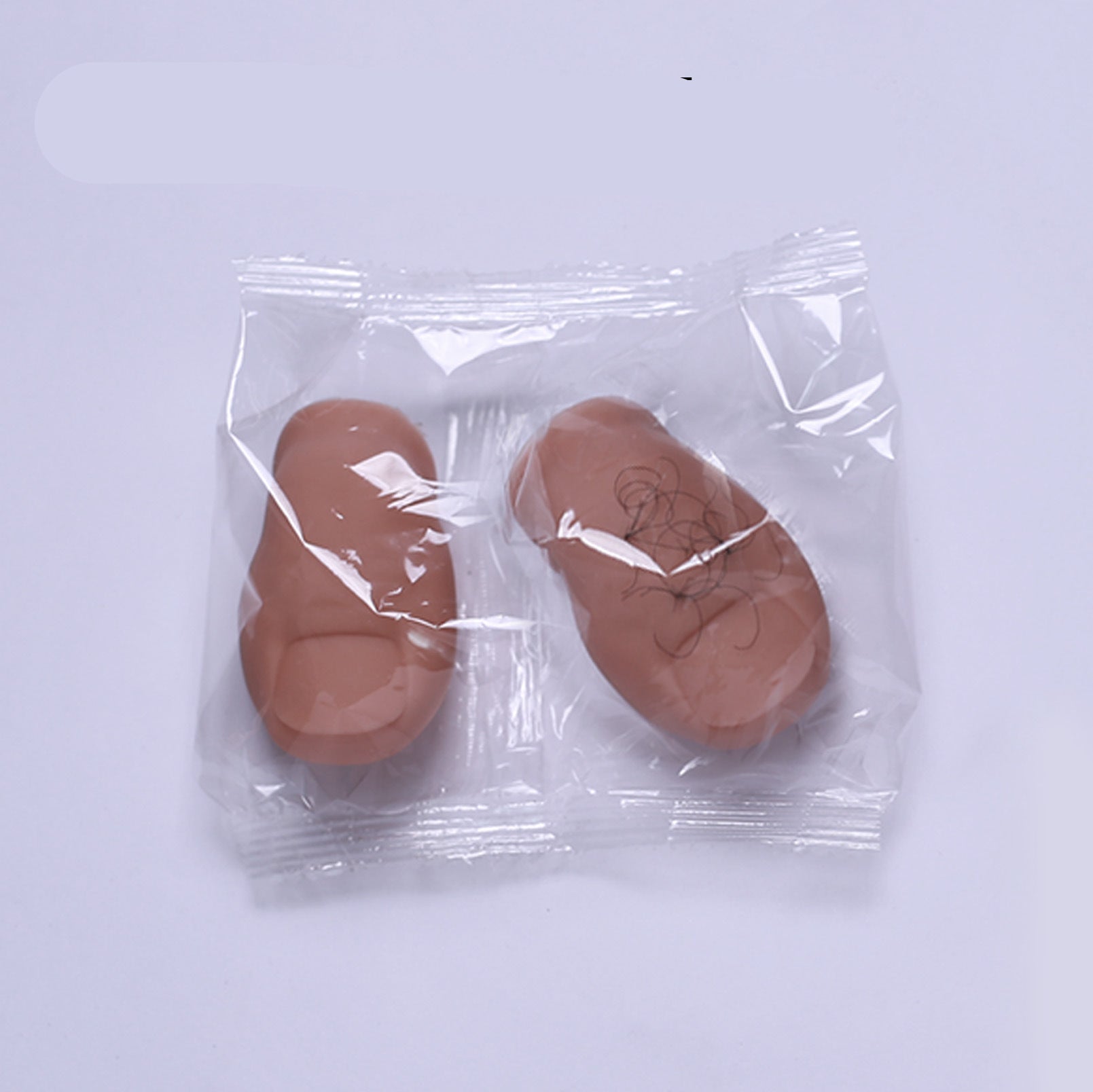 Two brown prosthetic halves in a clear plastic bag with 'Bald + Hairy' text above.