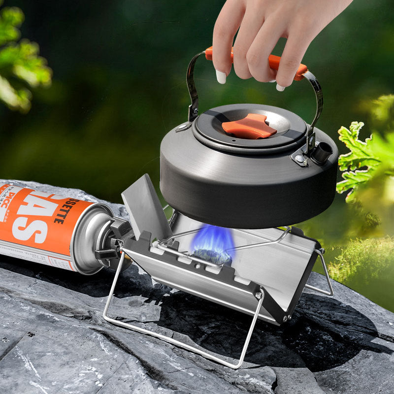 Person holding a camping kettle over a portable stove with a blurred natural background