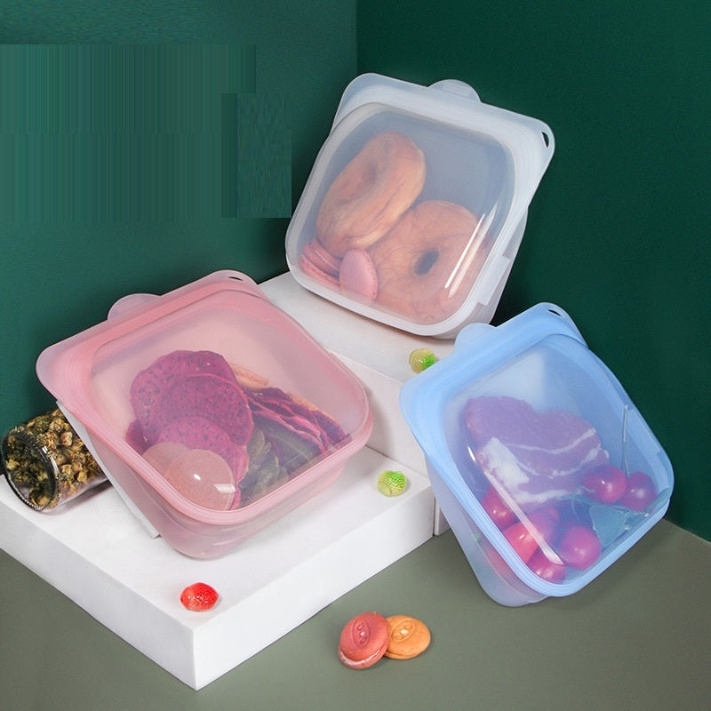 Three silicone food storage containers with food items on a white surface against a green background.