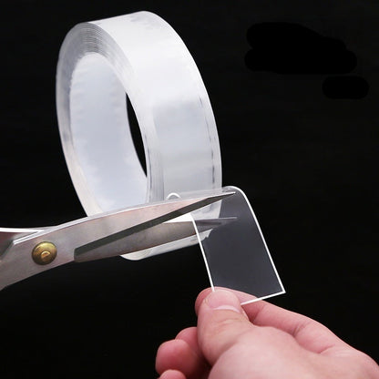 Clear tape with scissors and a hand holding a piece of clear material against a black background.