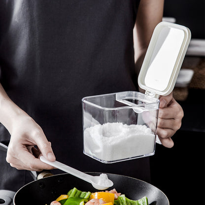 Person using a clear container with a white lid to add salt to food.