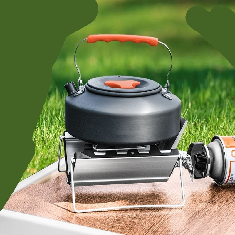 Black camping kettle with red handle on a stove over grass background