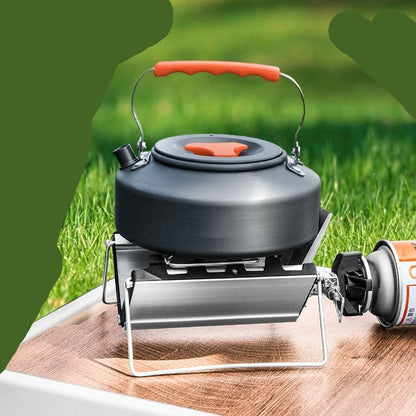 Black camping kettle with red handle on a stove over grass background