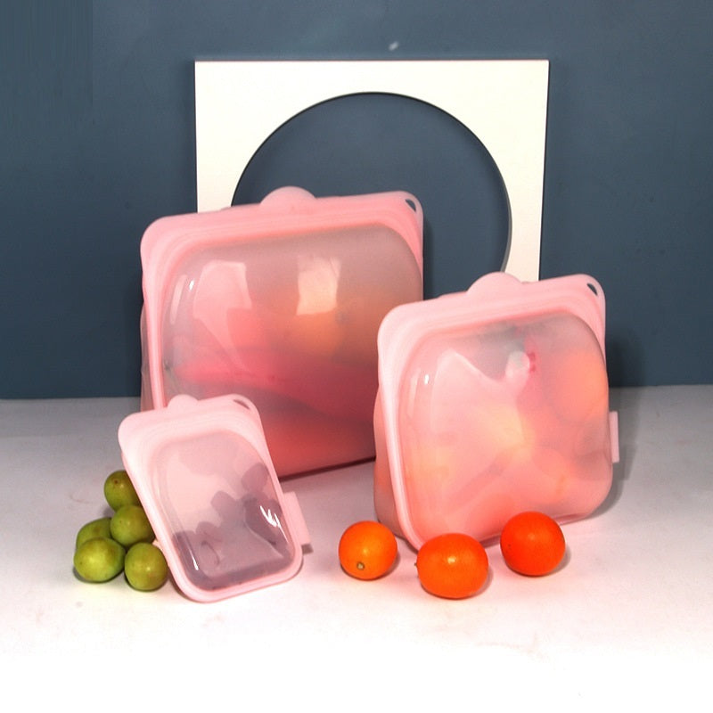 Pink silicone food containers with fruits on a white surface against a blue background